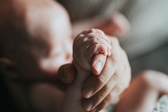 A newborn holding a parent's finger